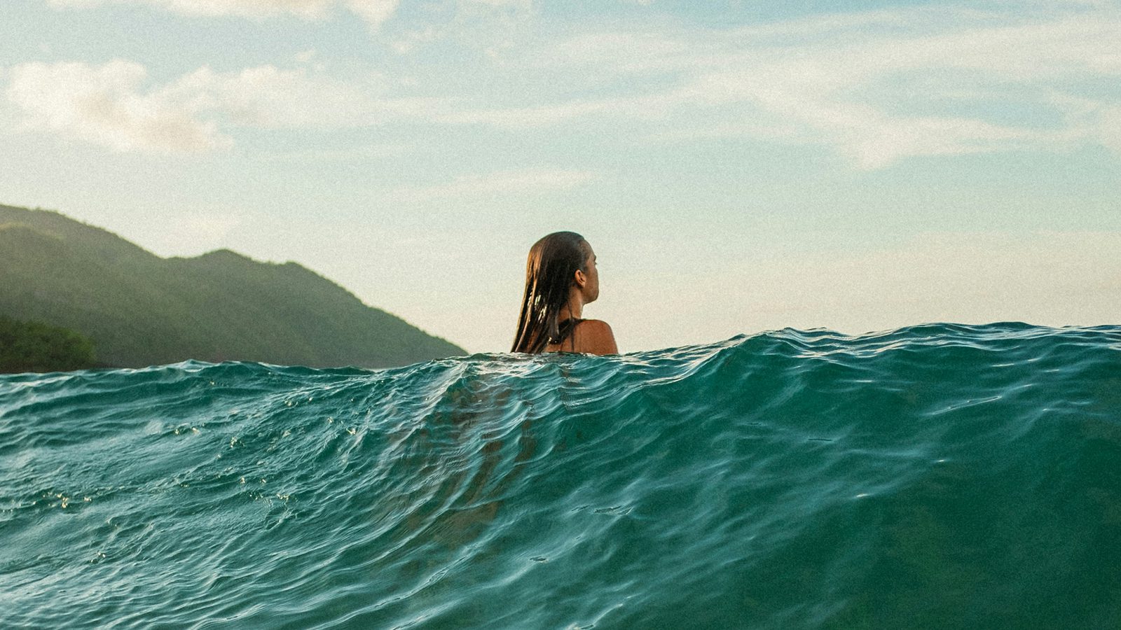 Woman standing in ocean waves looking toward distant mountains