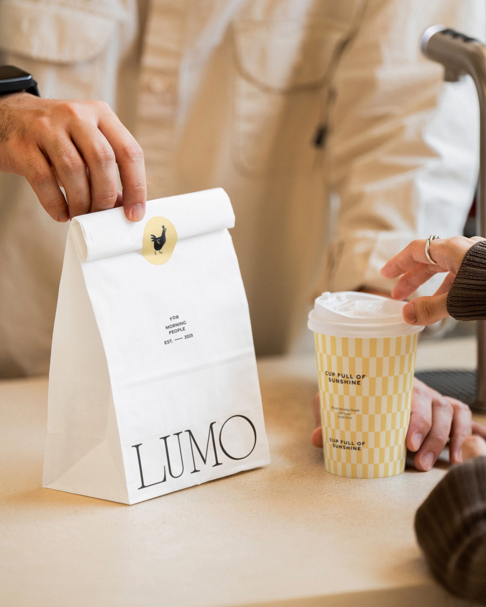 Hand placing a branded lumo paper bag on a counter next to a coffee cup